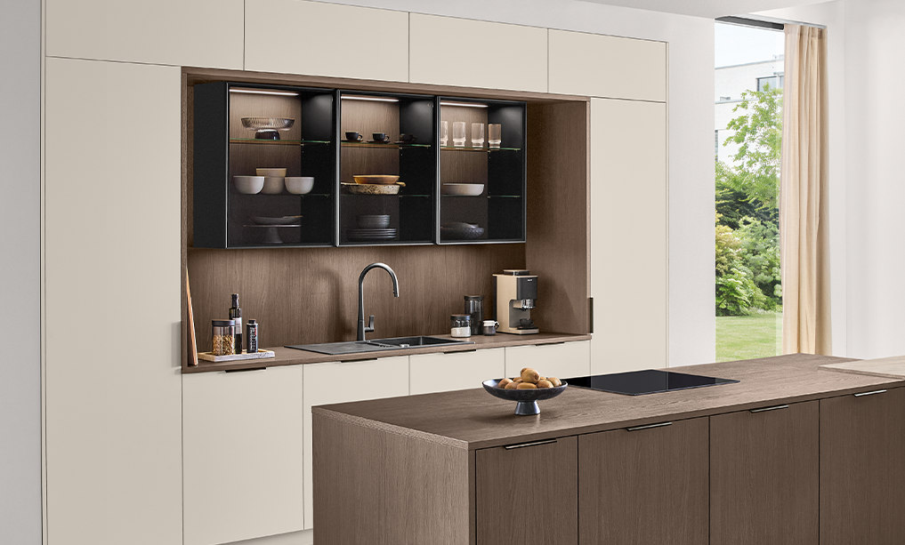 Helle Küche mit Fronten in Magnolia matt, dunkler Kücheninsel und Vitrinen mit Glastüren